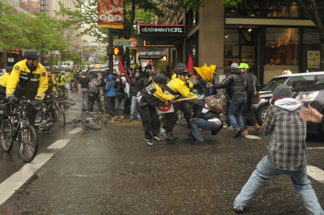 Three police peaceably subdue a citizen wielding a life threatening umbrella and sign on May Day 2012.  Photo by Pete Shaw